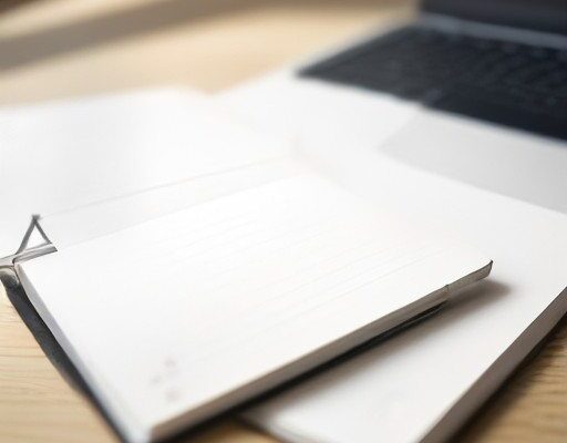 Scrivania con portatile e smartphone che mostrano un software per appunti accanto a un taccuino cartaceo